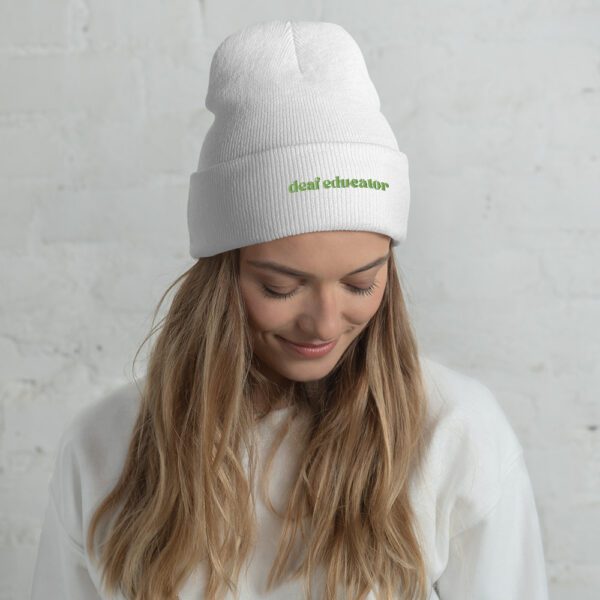 Person with long hair wearing white beanie with green "deaf educator" embroidery