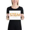 Female model holding a poster that shows "STEM" in orange with black illustrations.