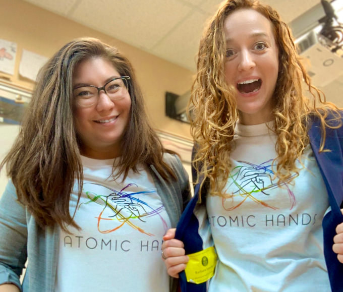 Alicia and Barbara smiling at the camera with their Atomic Hands shirts.